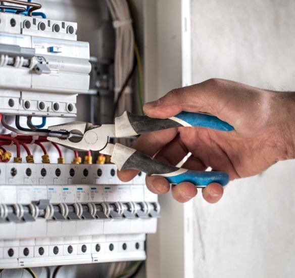 Man, an electrical technician working in a switchboard with fuses. Installation and connection of electrical equipment. Professional with tools in hand. concept of complex work, space for text.